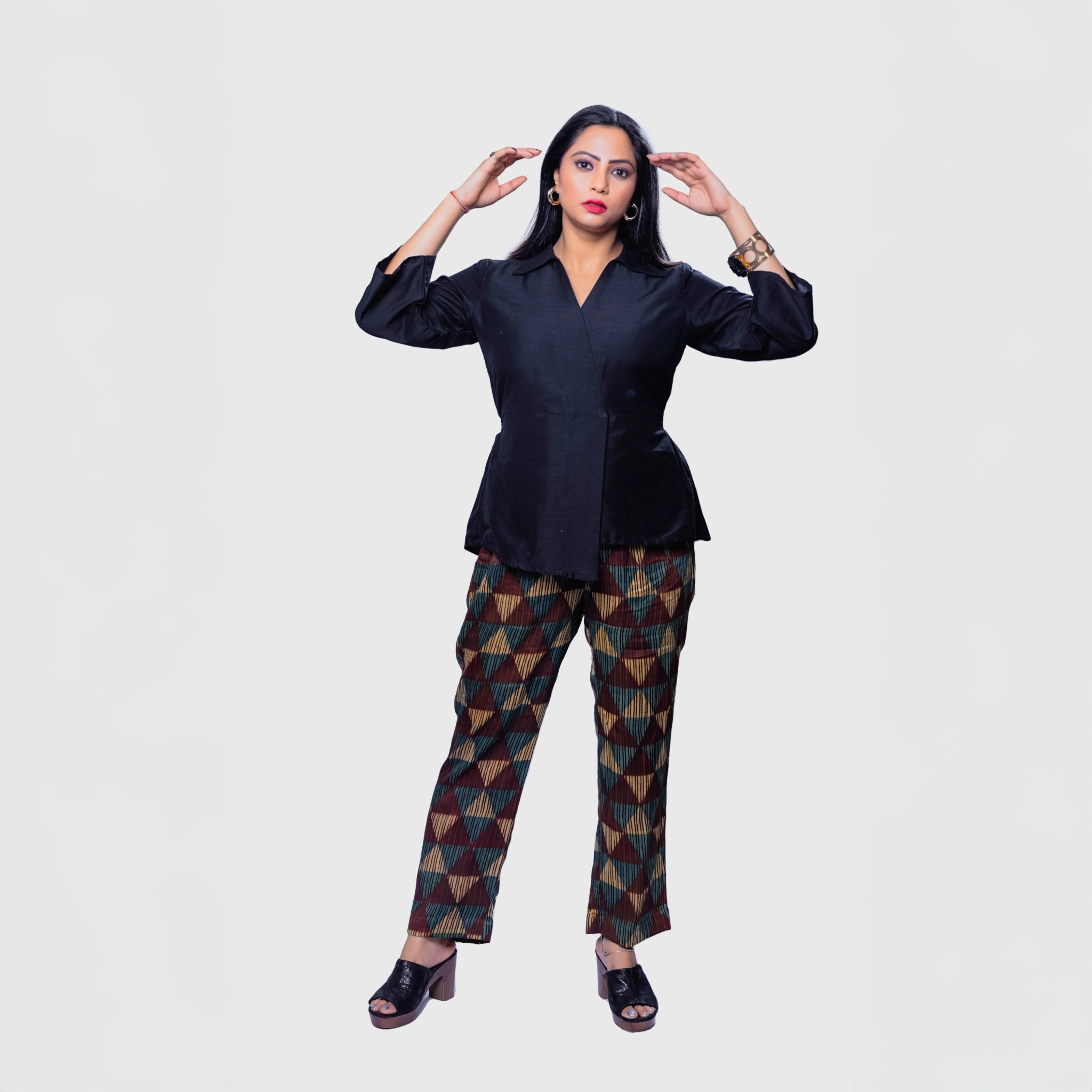 Woman wearing black collared top and pants set with geometric patterned pants and black heels