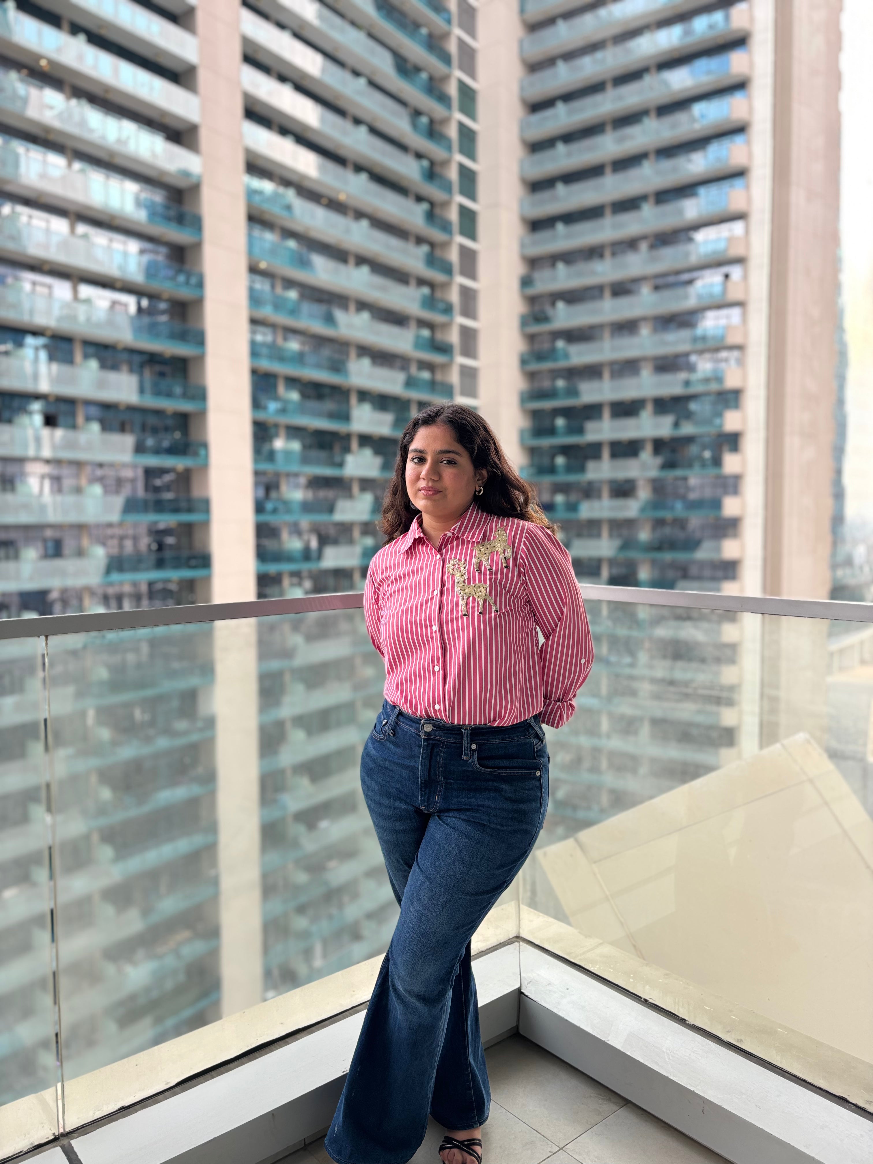 Stylish model wearing a pink striped sequin top for parties paired with flared jeans against a city backdrop