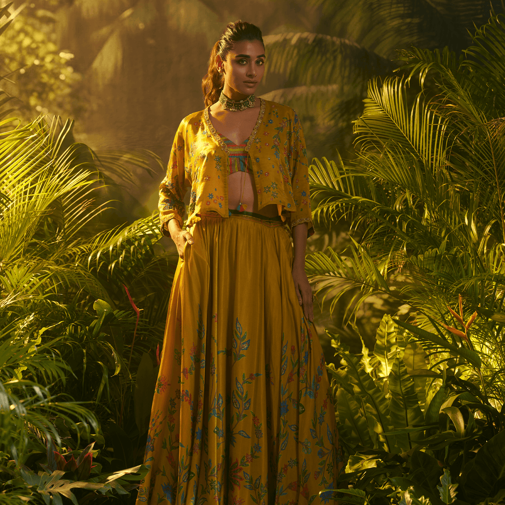 Elegant designer ghaghra choli with jacket in yellow floral pattern, surrounded by lush greenery