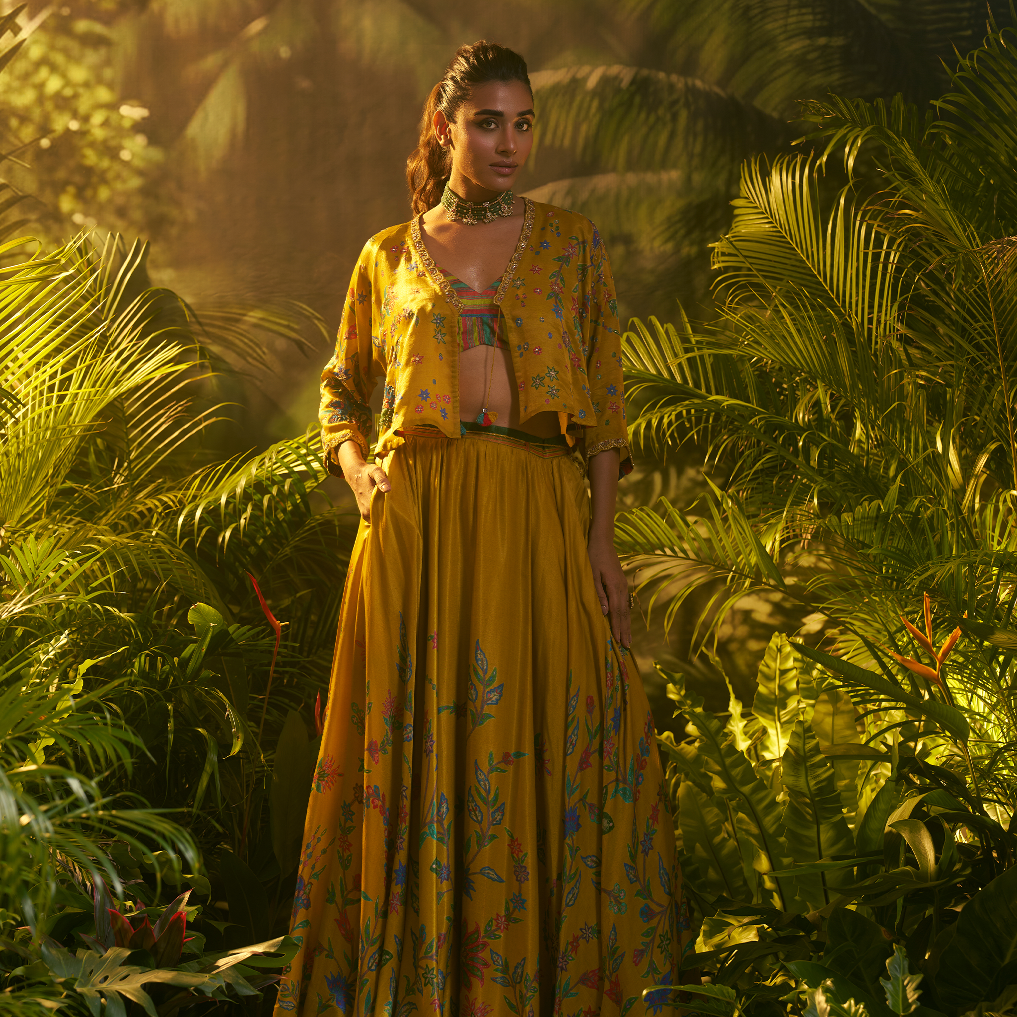 Elegant designer ghaghra choli with jacket in yellow floral pattern, surrounded by lush greenery