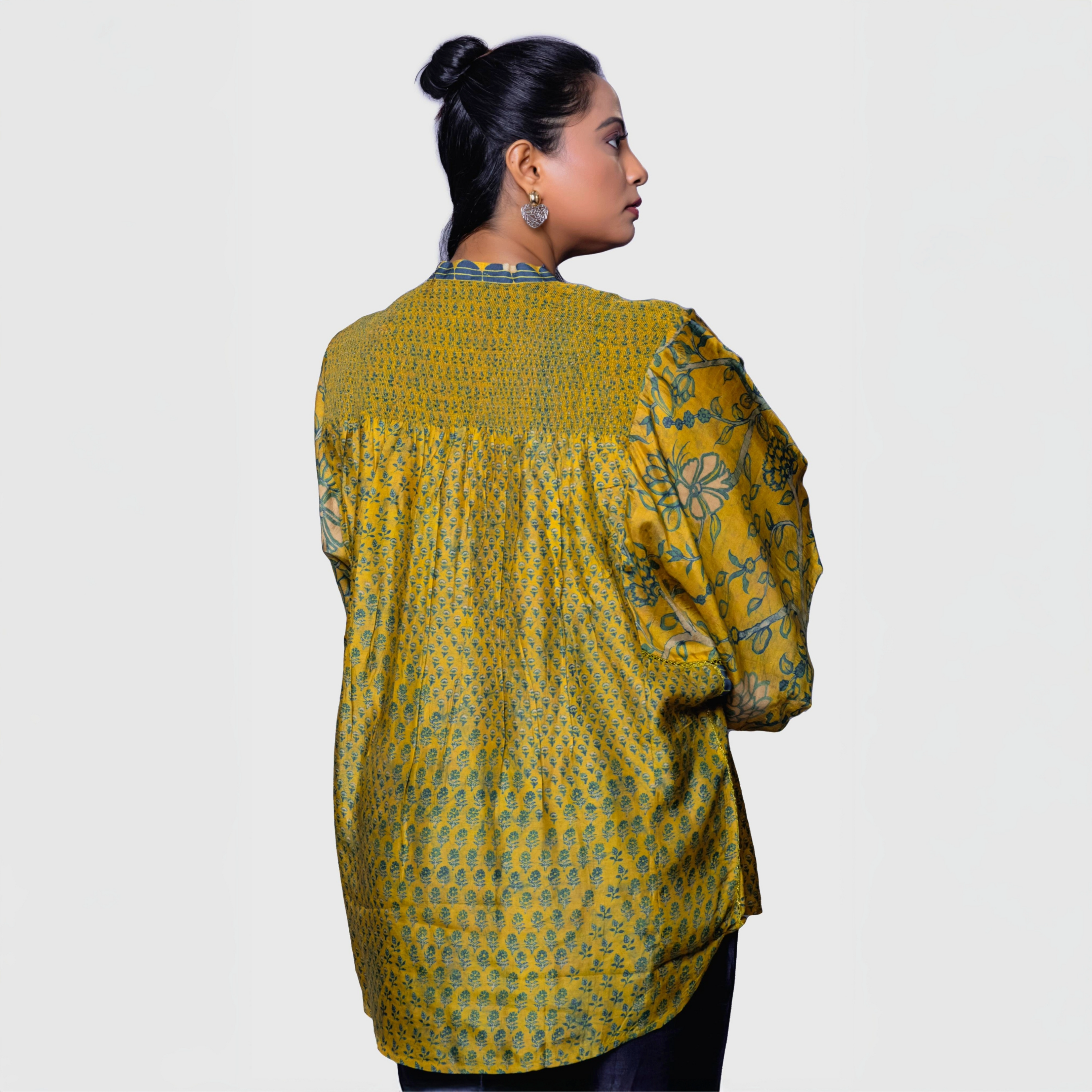 Back view of a woman wearing a mustard yellow fusion fashion Ajrakh shirt kaftan with floral and geometric patterns