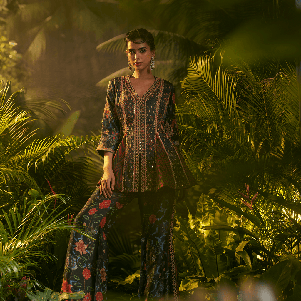 Model wearing a midnight bloom peplum ensemble with vibrant colors and intricate patterns in a lush setting