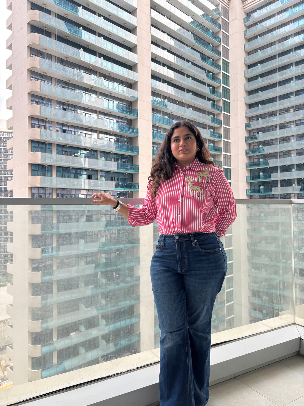 Pink striped sequin top for parties paired with flared jeans, model standing on a balcony